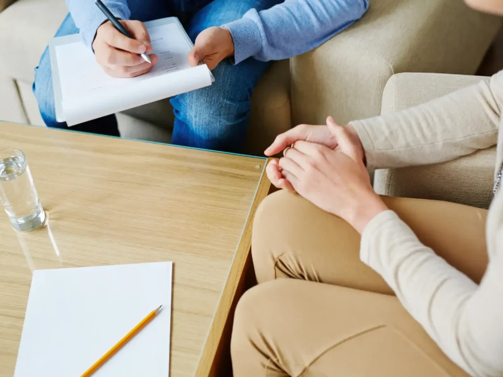 A person sits across from a therapist taking notes during a psychological assessment session in Los Angeles, with a blank sheet of paper and a pencil on the table, symbolizing the start of an evaluation process.